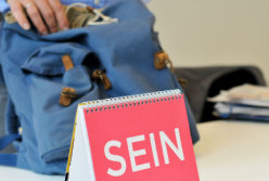 Dirk Addicks greift nach seinem Rucksack. Im Vordergrund ein Kalenderblatt mit der Aufschrift „SEIN“.